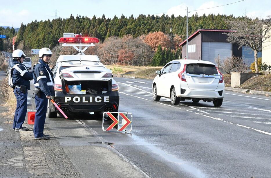 上北自動車道からみちのく有料道路に抜ける交差点付近で、八戸市方面からの車両を確認する警察官＝28日午前11時半過ぎ、七戸町後平（写真は一部加工しています）