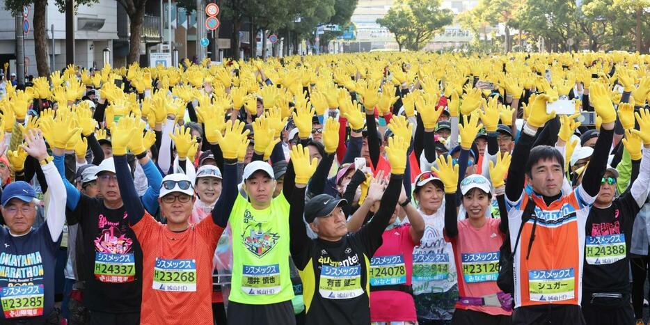 神戸マラソンのスタート地点で黄色い手袋を着け、両手を挙げるランナーたち＝２０２３年１１月１９日、神戸市中央区