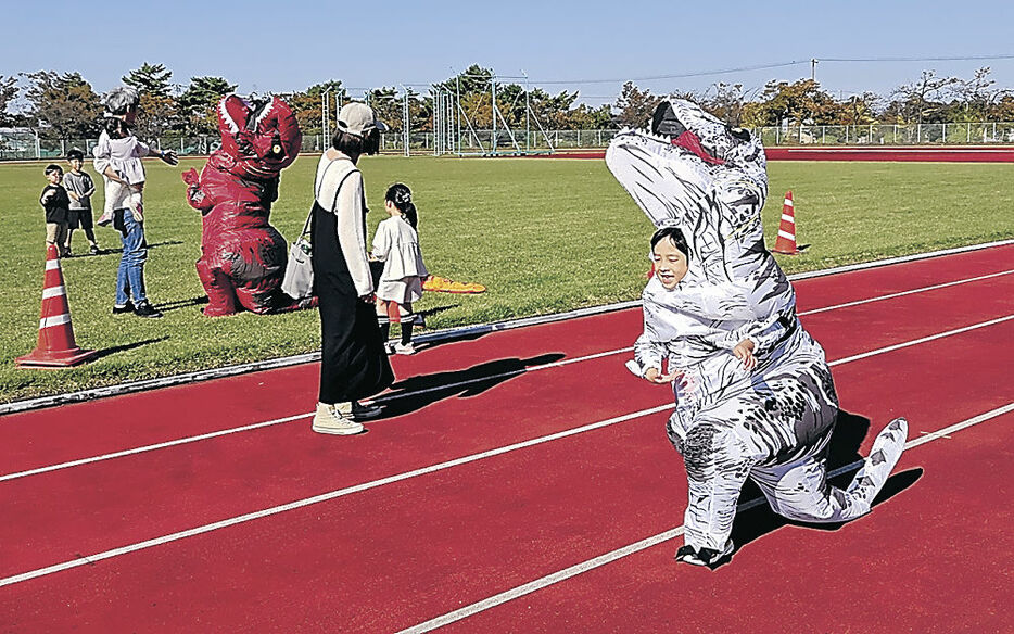 恐竜着ぐるみを着て走る子ども＝富山市の大沢野総合運動公園