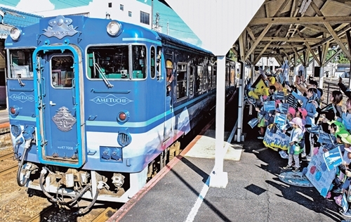 小旗を振って観光列車「あめつち」を見送る園児ら＝島根県雲南市木次町里方、木次駅