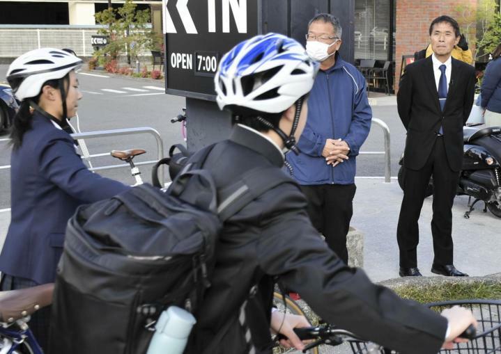 自転車通学の生徒のヘルメット着用状況を視察する宮崎北高校の玉城久裕教諭（右奥）＝25日朝、松山市湊町6丁目