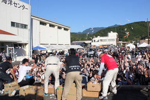 【恒例の餅まきに手を伸ばす見物客ら＝熊野市紀和町板屋の市紀和B＆G海洋センターで】