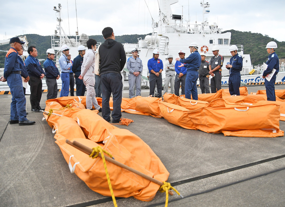 油流出事故に備えて陸上でオイルフェンスの取り扱い方を確認する参加者ら＝22日、鹿児島県奄美市名瀬