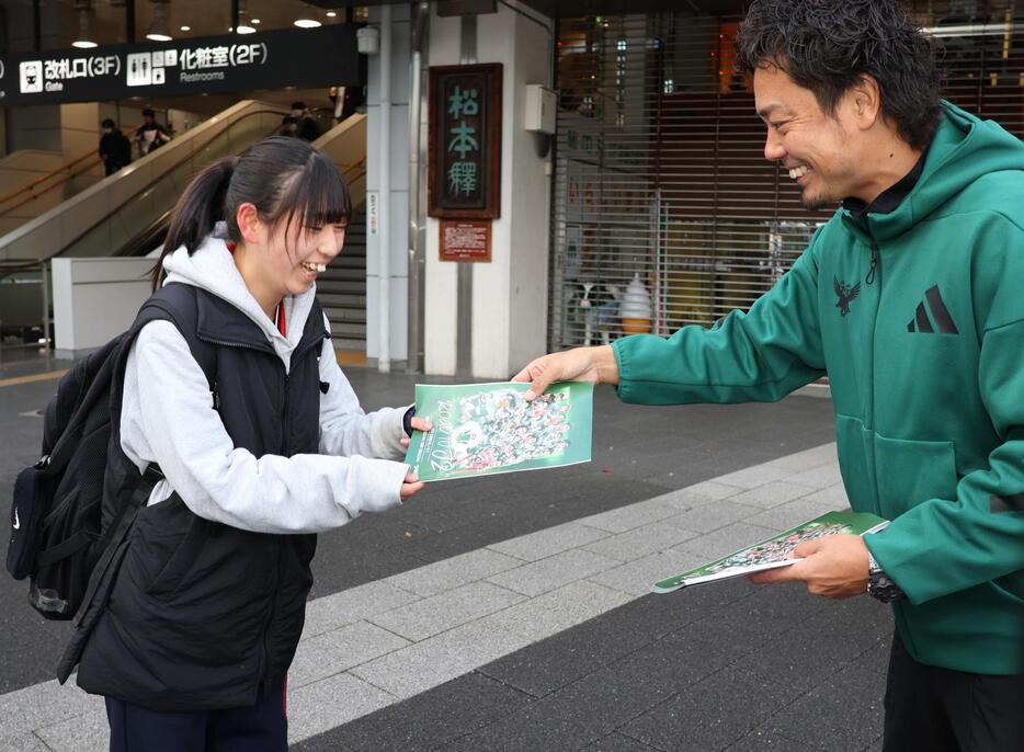 J2昇格プレーオフを知らせるチラシを受け取る駅利用者（左）