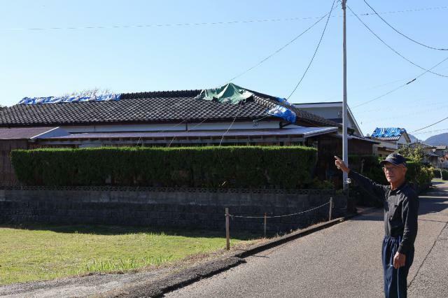 自宅を指さし、現状を説明する黒岩豊さん。地震から３カ月たつが、屋根にはシートがかけられたままだ＝６日午前、日南市平山