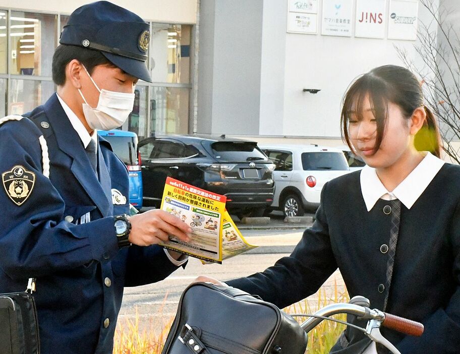 自転車で下校する高校生にチラシを配り、自転車の罰則強化について説明する青森署員（左）