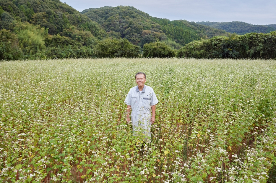 「常陸秋そばの郷まもりたい」の原種生産そば畑と関則史さん。9月末には一部が黒い実を付けていた