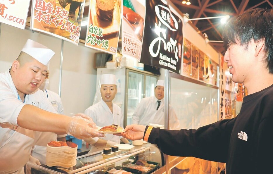 来場者に握りたてのすしを手渡す出店者