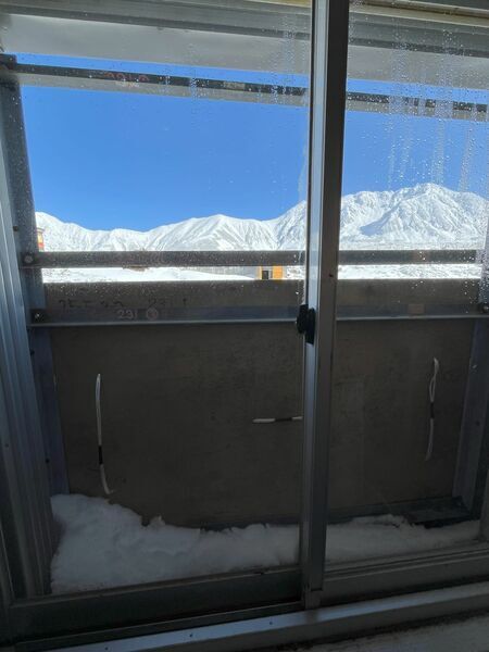 雪囲いで半分閉まった部屋の窓から望む山々