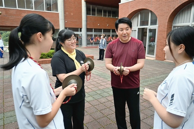 龍踊りで使う楽器の鳴らし方を教わる石川さん（左から2人目）と牧山さん（同3人目）