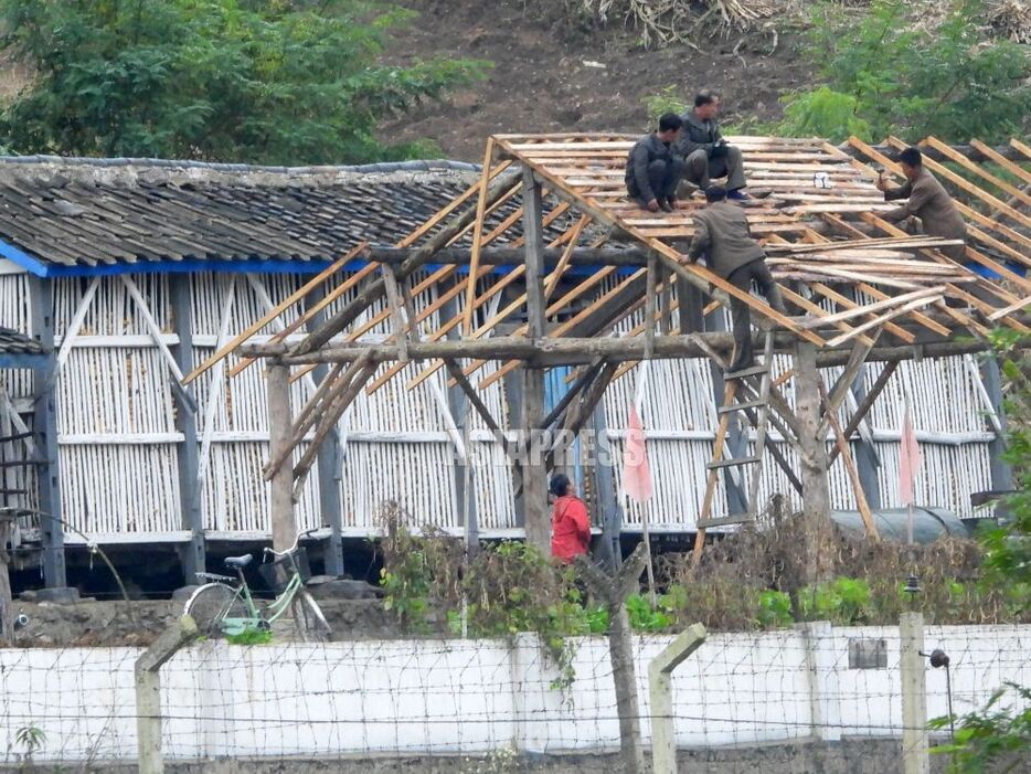 （クリックして拡大）奥の建物の隙間からトウモロコシが見える。農場の保管庫だろう。屋根で作業しているのは農場員だと思われる。7月末の水害で流された農場の施設を建て直しているのか。