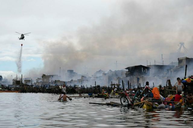 フィリピンの首都マニラで2024年11月24日、炎上する住宅に向けて放水する空軍のヘリコプター=AP