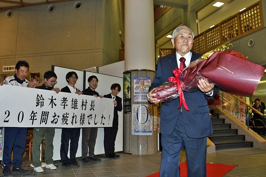 職員から贈られた花束を手に、退庁する鈴木村長＝15日、田舎館村役場