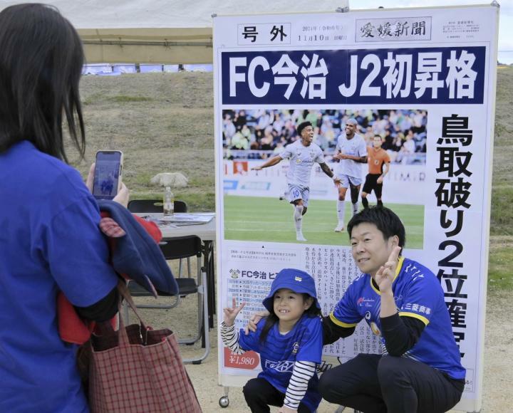 FC今治のJ2昇格を祝い、巨大号外の前で記念撮影する来場者＝24日午前、今治市のアシックス里山スタジアム（撮影・多田良介）