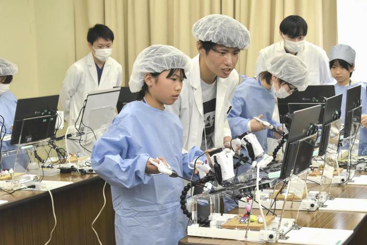 医師のブースで、腹腔（ふくくう）鏡手術の練習に使う機器を操作し、菓子や小物を動かす参加者