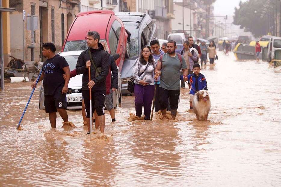 10月30日、スペイン東部バレンシアで冠水し、車が折り重なる道路を歩く人たち（AP）