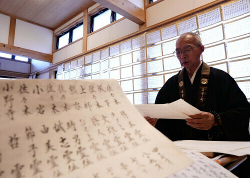 犠牲者の氏名が書かれた半紙を前にお経を上げる高橋住職（１７日、陸前高田市で）＝広瀬航太郎撮影