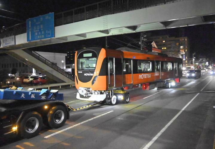 けん引車に引かれ、味酒小学校前の歩道橋の下を通る伊予鉄の新車両＝6日午後11時10分ごろ、松山市宮西2丁目