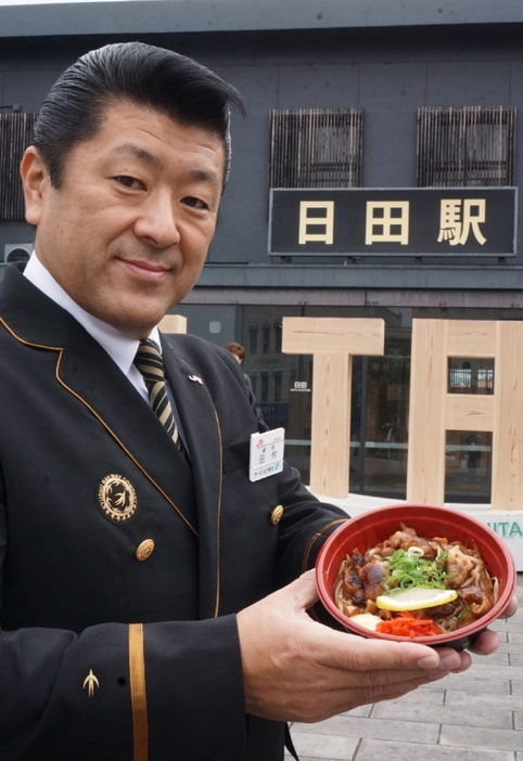 「福地のうなるホルモン丼」を推す田村直樹日田駅長＝日田市のJR日田駅前