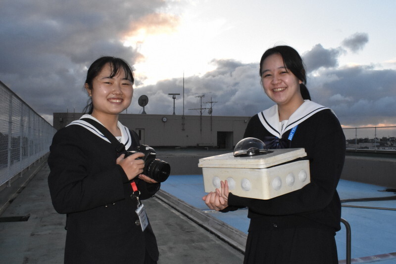 福岡工業大付属城東高の屋上で観測装置やカメラを手にする野崎芙悠さん（右）と刀根佳子さん＝福岡市東区で2024年11月18日、山崎あずさ撮影