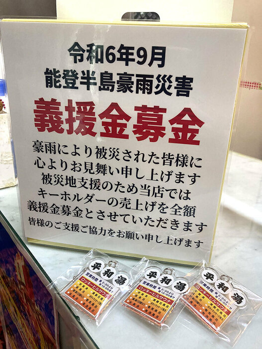 番台に置かれた募金箱と１００個用意したオリジナルキーホルダー＝川崎市川崎区の平和湯