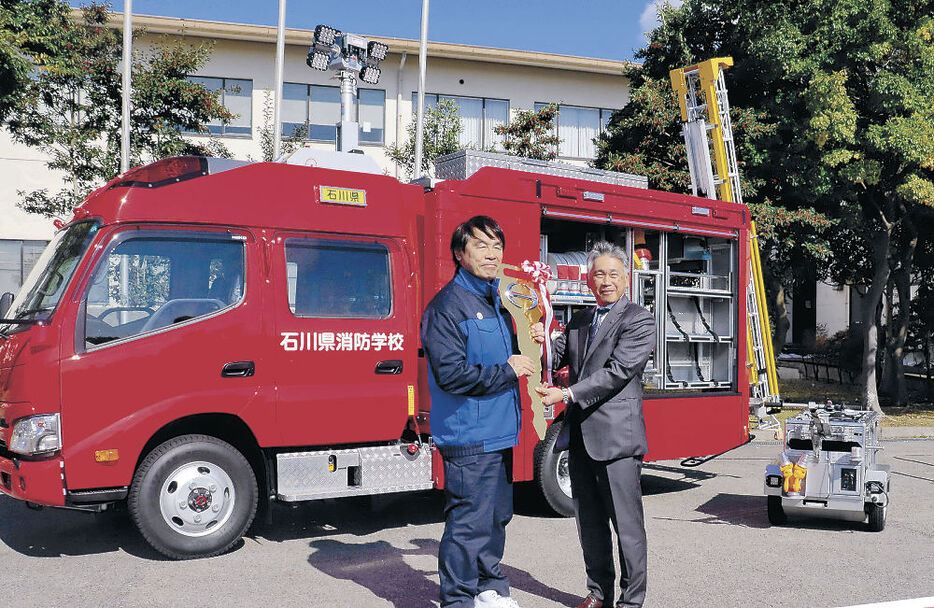 軽量素材を採用した消防ポンプ車の前で馳知事（左）にレプリカキーを手渡す長野社長＝県消防学校