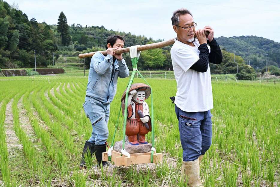 下狩宿の住民に担がれ、稲刈り後の田んぼを見回る田の神＝１９日午後、さつま町求名