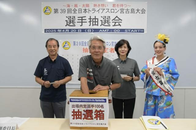 抽選箱から選手を選ぶ座喜味市長ら＝12日、市役所