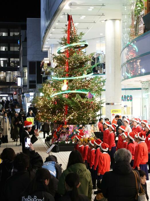 点灯したクリスマスツリーの前で合唱する子どもたち