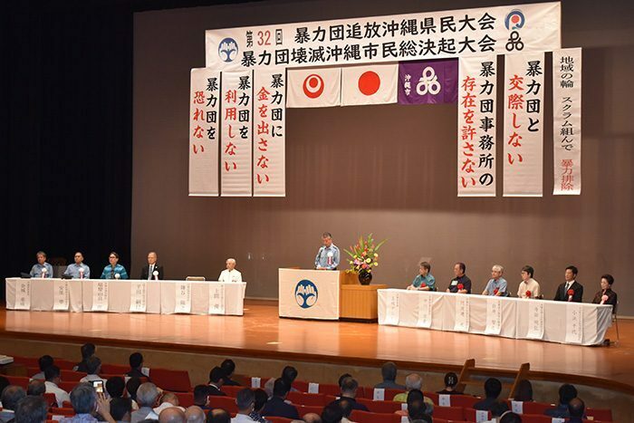 反社会的勢力の排除に向けて協力を呼び掛ける鎌谷陽之県警本部長のあいさつに耳を傾ける聴衆ら＝15日、沖縄市八重島の沖縄市民会館