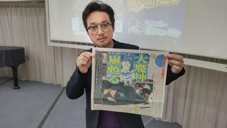 世田谷区立中央図書館で講演会を行い、漫画が書かれた日刊スポーツを手にするやくみつるさん