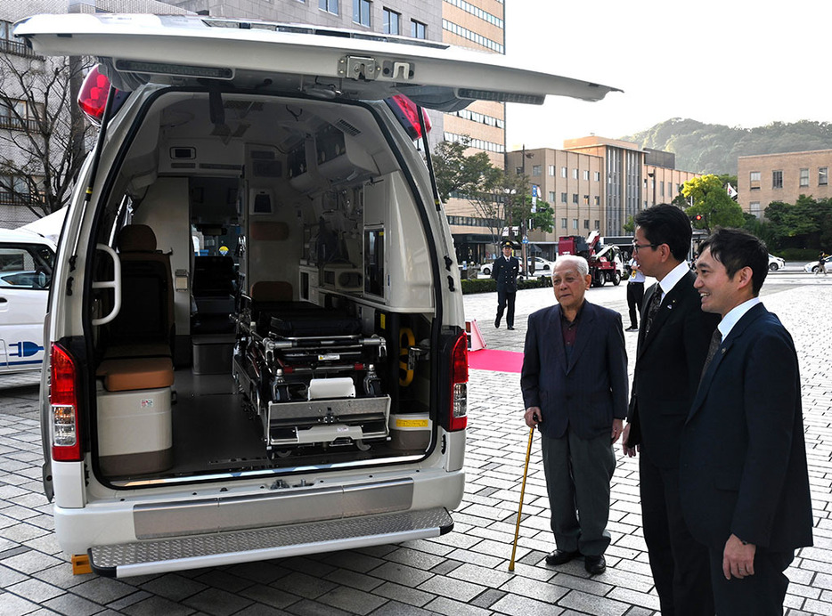 才納さん（左端）が寄贈した救急車を案内する下鶴市長（中央）