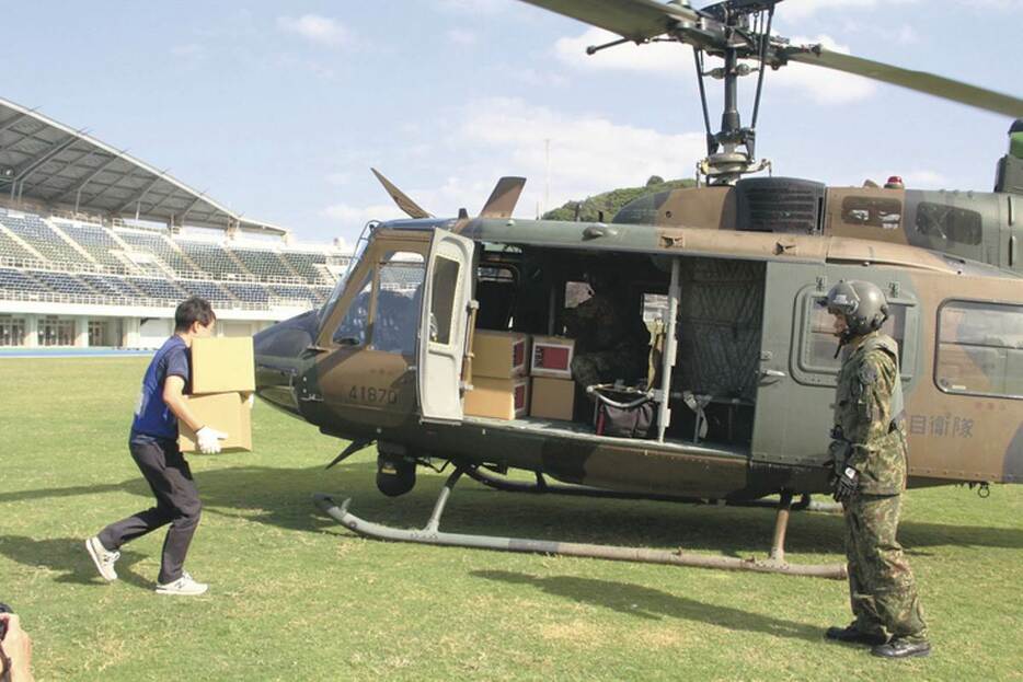 陸上競技場に着陸した陸上自衛隊のヘリコプターに積むために段ボールを運ぶ参加者＝13日、下関市向洋町