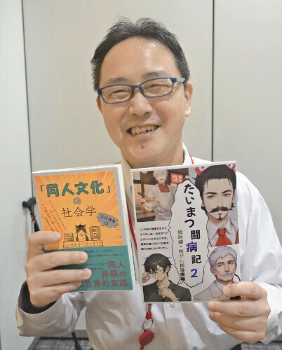 吉本たいまつさん。左手に持っているのは、自らのがん闘病記を漫画にした同人誌