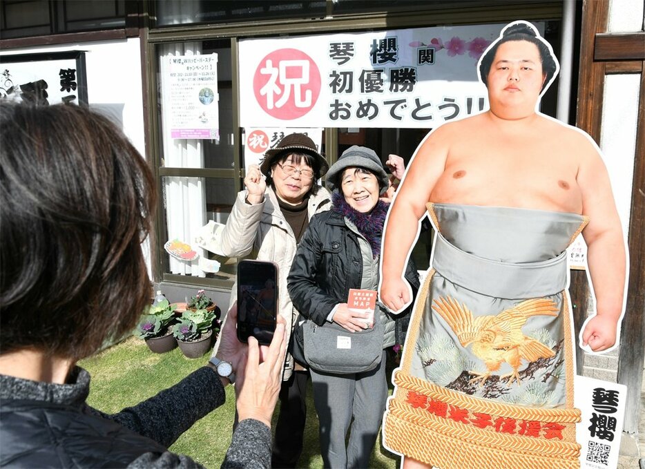 初優勝を祝う横断幕の前で等身大パネルと並んで写真を撮影する相撲ファンら＝２５日、倉吉市魚町の琴桜記念館