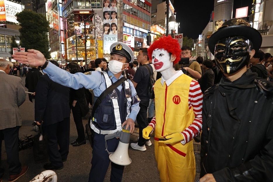 ハロウィーン当日を迎え、東京・渋谷のスクランブル交差点付近で仮装した人に道を問われる警察官＝10月31日夜