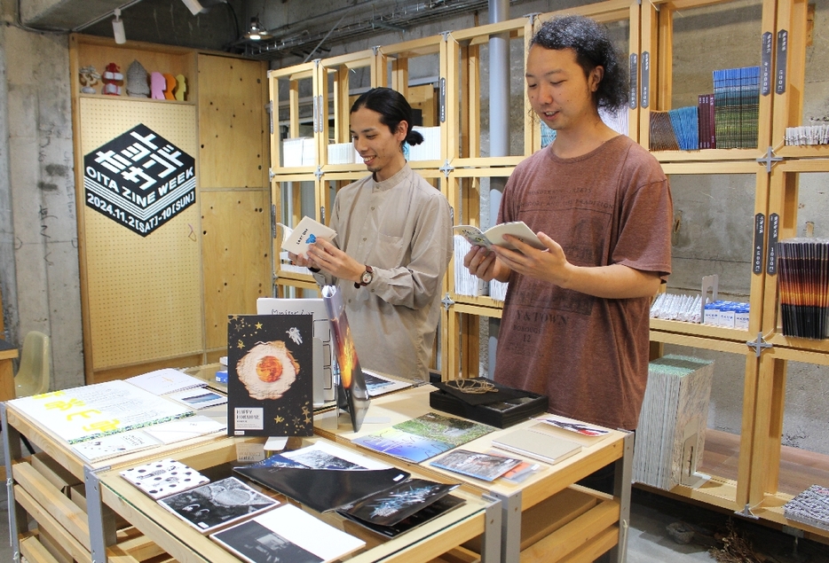 「ZINE」を手に取る羽山仁史さん（右）と佐藤寿喜さん＝大分市府内町のmazeru