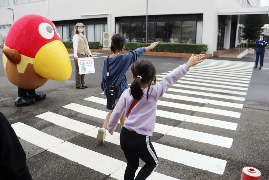 人気キャラクター「キョロちゃん」（左）が見守る中、横断歩道を渡る小学生＝15日午前、横浜市