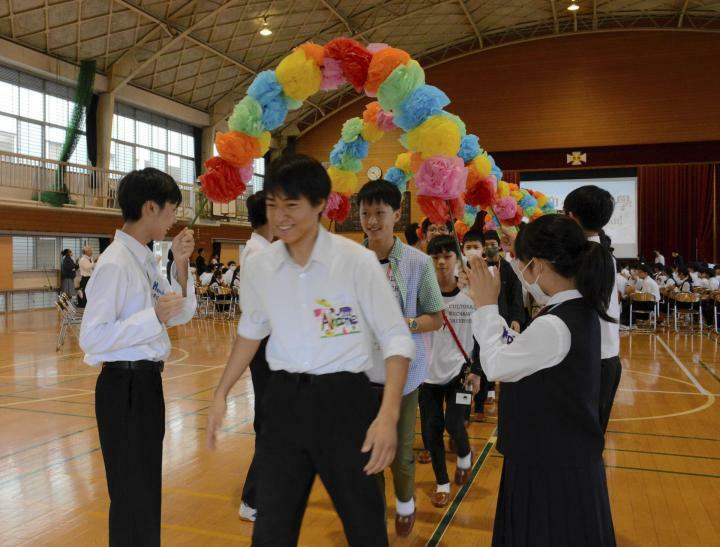 松山市東中でのウェルカム集会で、花のアーチを通って各クラスに向かう介寿中生＝1日午前、同市文京町