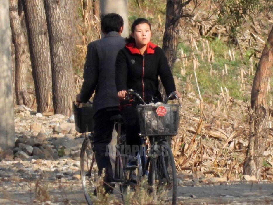 （クリックして拡大）女性が乗る自転車の前かごには、「満浦」と居住地を示す登録証がつけられている。