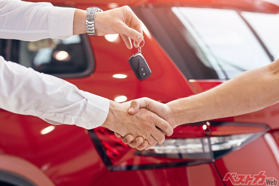 Unrecognizable manager shaking hand of customer and handing keys while sealing deal in car dealership