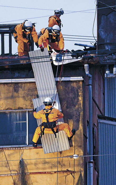 屋上から宙づりとなり、壁面のトタンを撤去する消防隊員＝金沢市笠舞３丁目