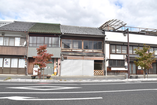 広小路通りに面する元駐車場の建物（中央）。奥に古民家がある