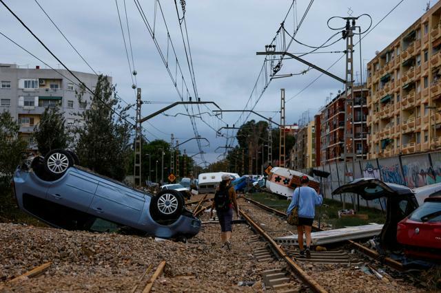 スペイン東部バレンシア州アルファファルで2024年10月31日、線路沿いに流された車の脇をほうきを持って通り過ぎる女性たち=ロイター