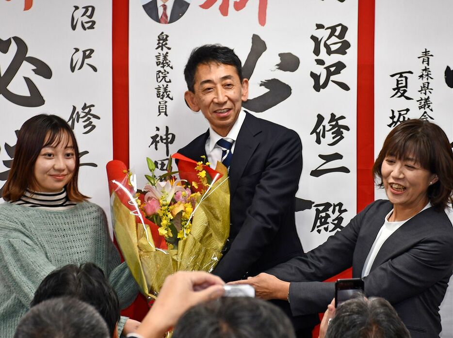 娘のはなさん（左）から花束を受け取り、喜ぶ沼沢氏。右は妻の弘子さん＝17日午後8時22分、三戸町川守田沖中の事務所