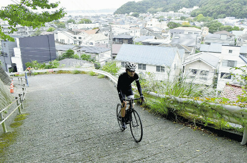 教会への激坂を上る長谷川さん（手前）。坂の途中からは相模湾も見渡せる（葉山町で）