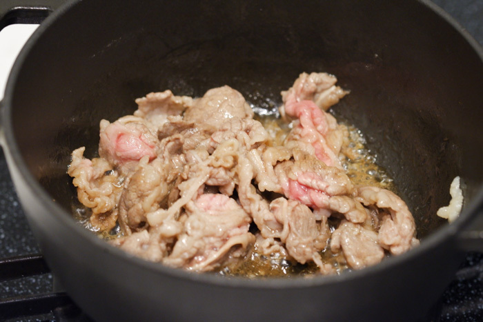 2．鍋にごま油を熱し、牛こま肉、おろしにんにく、焼き肉のたれを入れて牛肉の色が変わるまで炒める。