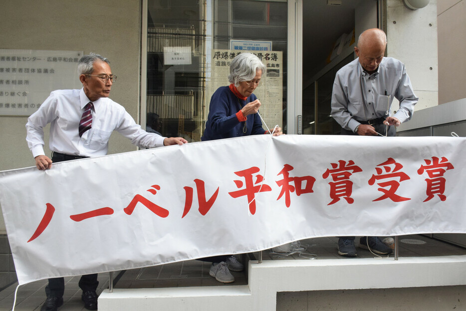 日本原水爆被害者団体協議会のノーベル平和賞受賞決定を祝う横断幕を掲示する箕牧智之代表委員（右端）ら＝５日午後、広島市中区