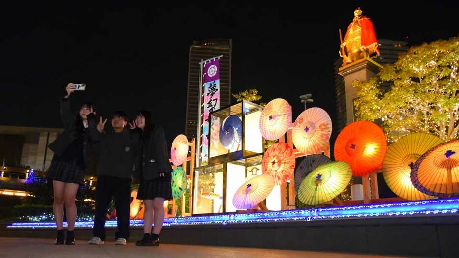 ライトアップされた和傘の前で写真を撮る人たち＝１５日午後８時９分、岐阜市橋本町、ＪＲ岐阜駅北口信長ゆめ広場（撮影・坂井萌香）