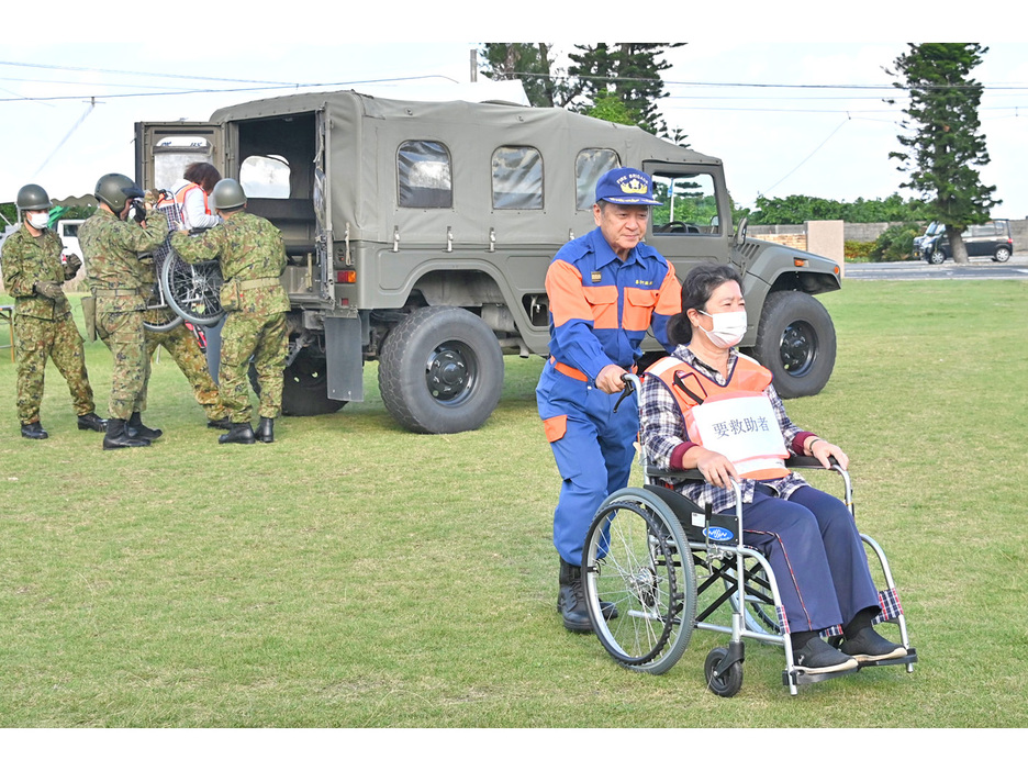 浸水で孤立した地区から自衛隊車両で運ばれた要救助者と、搬送にあたる消防署員＝23日、鹿児島県喜界町